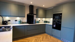 A modern kitchen with grey cabinets, a black range hood, a built-in microwave, and a herringbone-patterned wooden floor. - Cozy Bedford Home with 3 Bedrooms (Bedford)