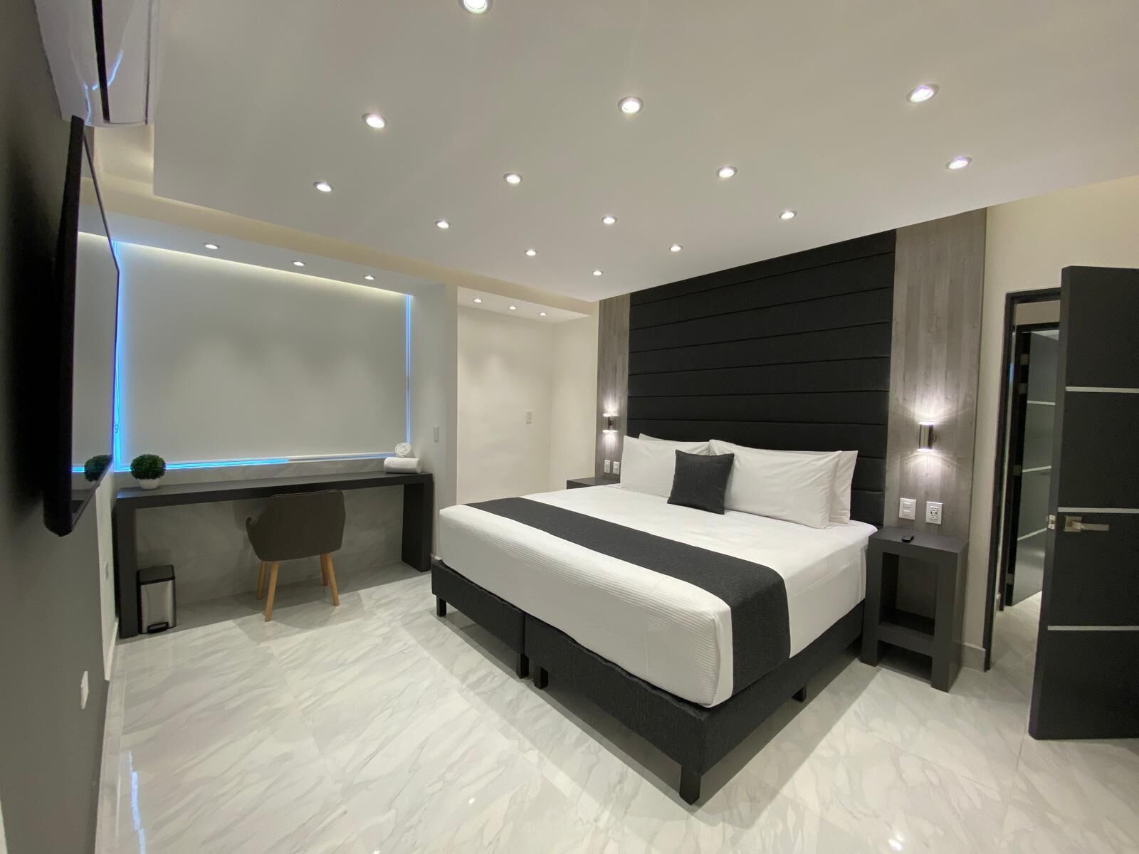 A modern bedroom with a large bed, bedside tables, a desk, and a mirror.