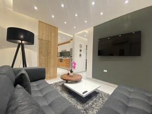 Ein modernes Wohnzimmer mit einer Couch, einem Couchtisch, einer Lampe und einem an der Wand befestigten Fernseher.