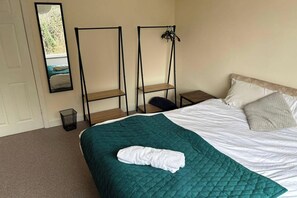 Ein Schlafzimmer mit einem Bett, einer grünen gesteppten Bettdecke, einem weißen Kopfkissen, einem hölzernen Nachttisch und einem schwarzen Metallregal.