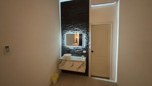 A small bathroom with a marble vanity, a black textured wall, a white door, and a yellow trash bin.