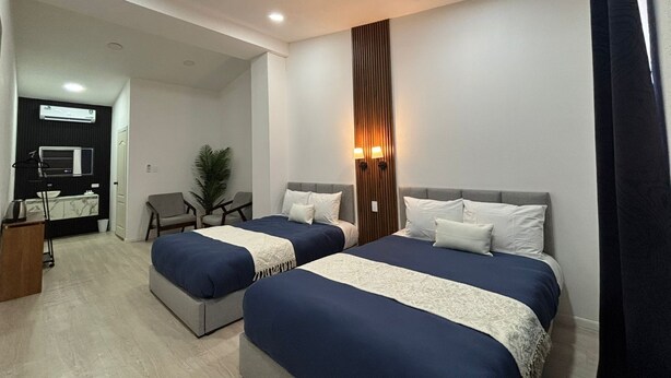 A hotel room with two beds, a desk, a chair, and a potted plant.