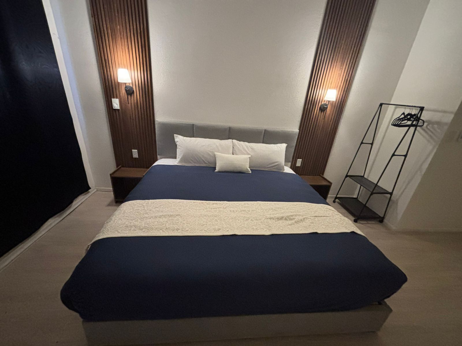 A neatly made bed with a blue and white bedspread, flanked by wooden headboards with wall-mounted lights.