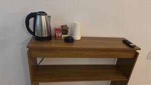 A wooden desk with a kettle, a coffee maker, a remote control, and some cups.