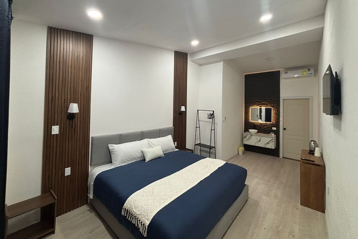 A modern bedroom with a large bed, a bedside table, a mirror, and a TV mounted on the wall.