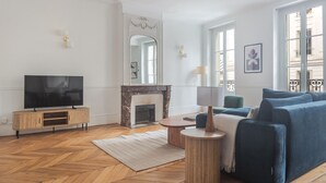 A spacious living room with a large flat-screen TV, a fireplace, and a comfortable seating area with a sofa and armchairs. - Blueground | Épinettes, view, nr Parc Monceau (Paris)