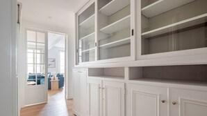 A hallway with white cabinetry and a view into a living area with a blue sofa and a round wooden table. - Blueground | Épinettes, view, nr Parc Monceau (Paris)