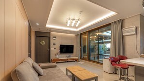A modern living room with a sofa, coffee table, TV, and a dining area with red chairs. - Jeju Calma (Jeju City)