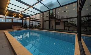 Ein Hallenbad mit Glasdach, eine Sonnenterrasse mit Sitzgelegenheiten und Blick auf die umliegende Landschaft.