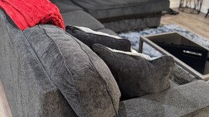 Un saló modern amb un sofà seccional gris, una manta vermella i una taula petita negra.