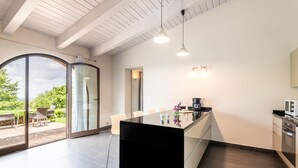 A modern kitchen with a large island, sliding glass doors leading to an outdoor area, and a dining table with chairs. - Luxurious home in Trequanda with house a panoramic view (Trequanda)