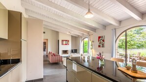 A modern kitchen with a large island, a dining area with a table and chairs, and a view of greenery outside. - Luxurious home in Trequanda with house a panoramic view (Trequanda)