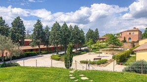 Un patio con un sendero de grava, rodeado de árboles y edificios con techos de tejas rojas.