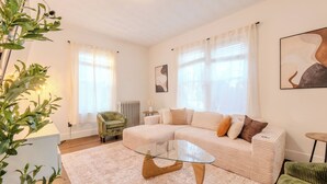 Un salon moderne avec un canapé d’angle, une table basse en verre, un fauteuil vert et une plante en pot.