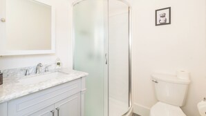Une salle de bain avec une douche à parois de verre, un lavabo blanc doté d’un plan de toilette en marbre et des toilettes.