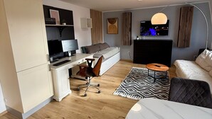 Un apartamento moderno con cocina, comedor y sala de estar. Incluye un escritorio, silla, sofá y televisor.
