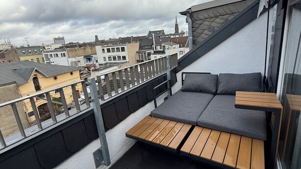 Una terraza en la azotea con cubierta de madera, sofá gris y una pequeña mesa de madera.