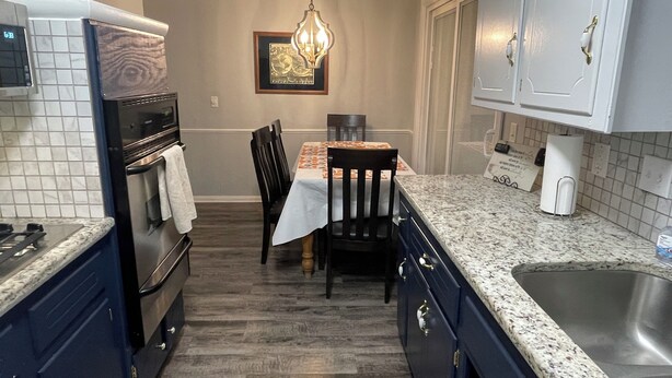 A kitchen with dark blue cabinets, a granite countertop, a dining table with a white tablecloth, and a hanging light fixture. - Aimee's Place- Comfy and  Close to Everything! (Moore)