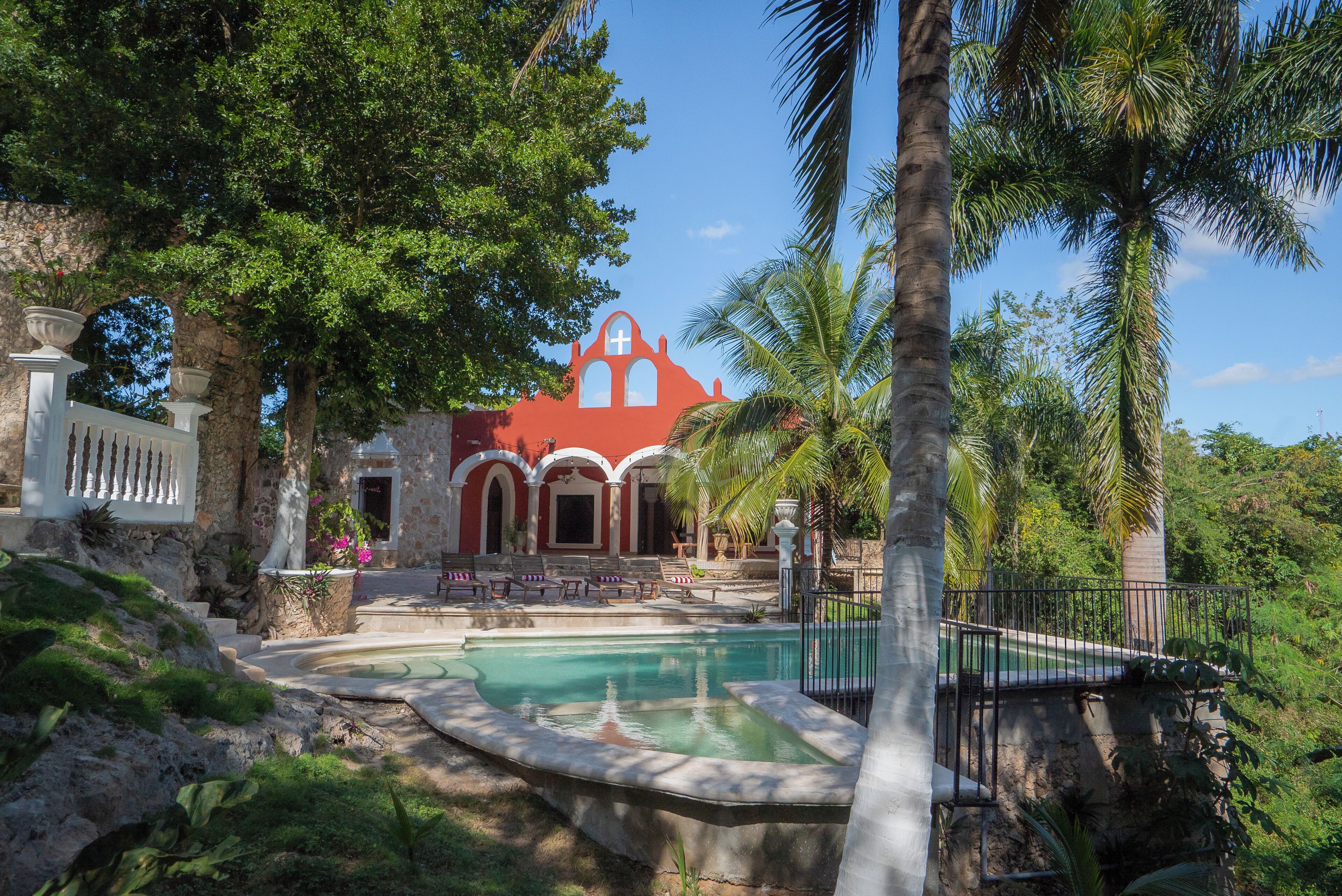 A pool area with a red building, palm trees, and a stone wall.