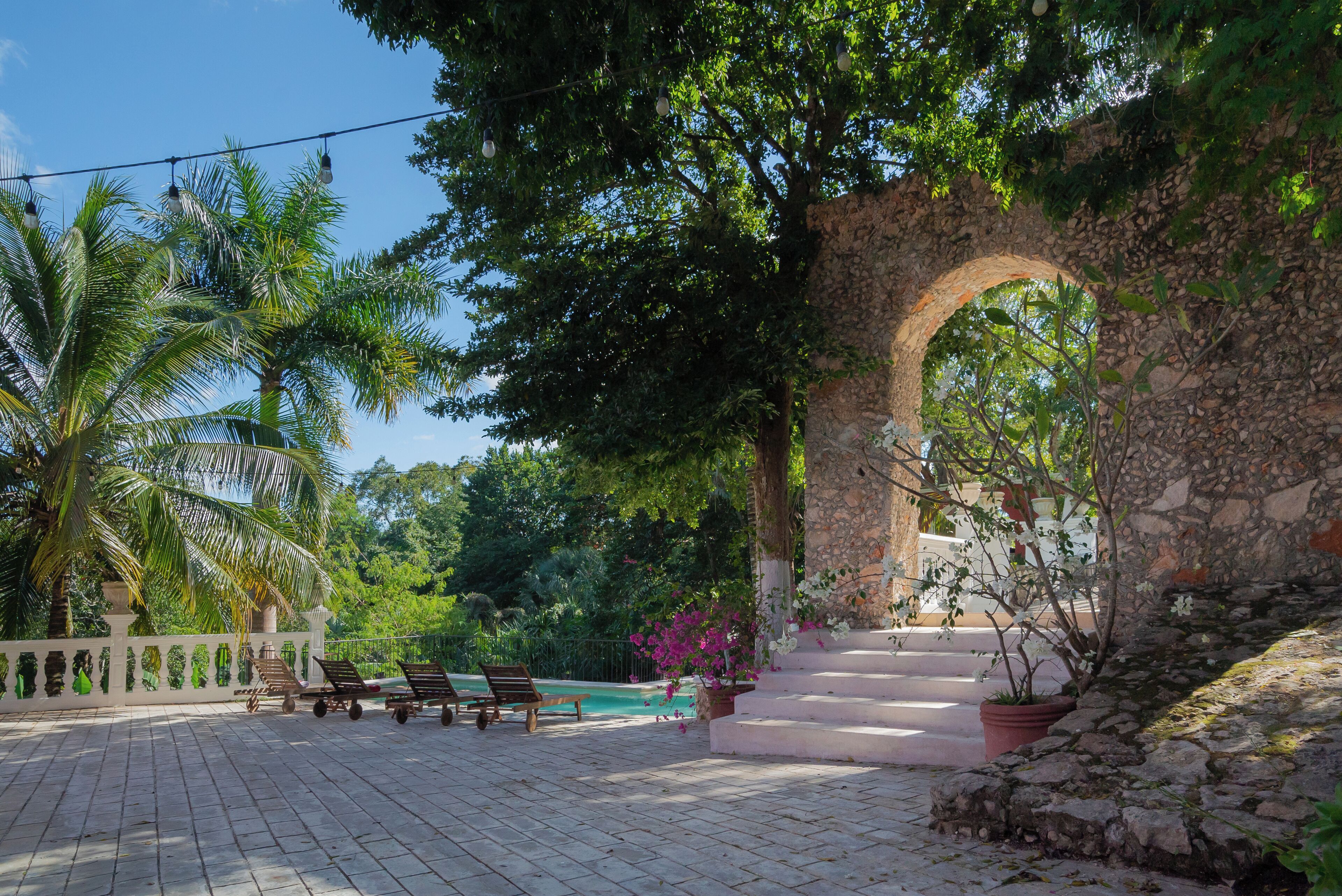 A courtyard with a stone archway, palm trees, and a pool.