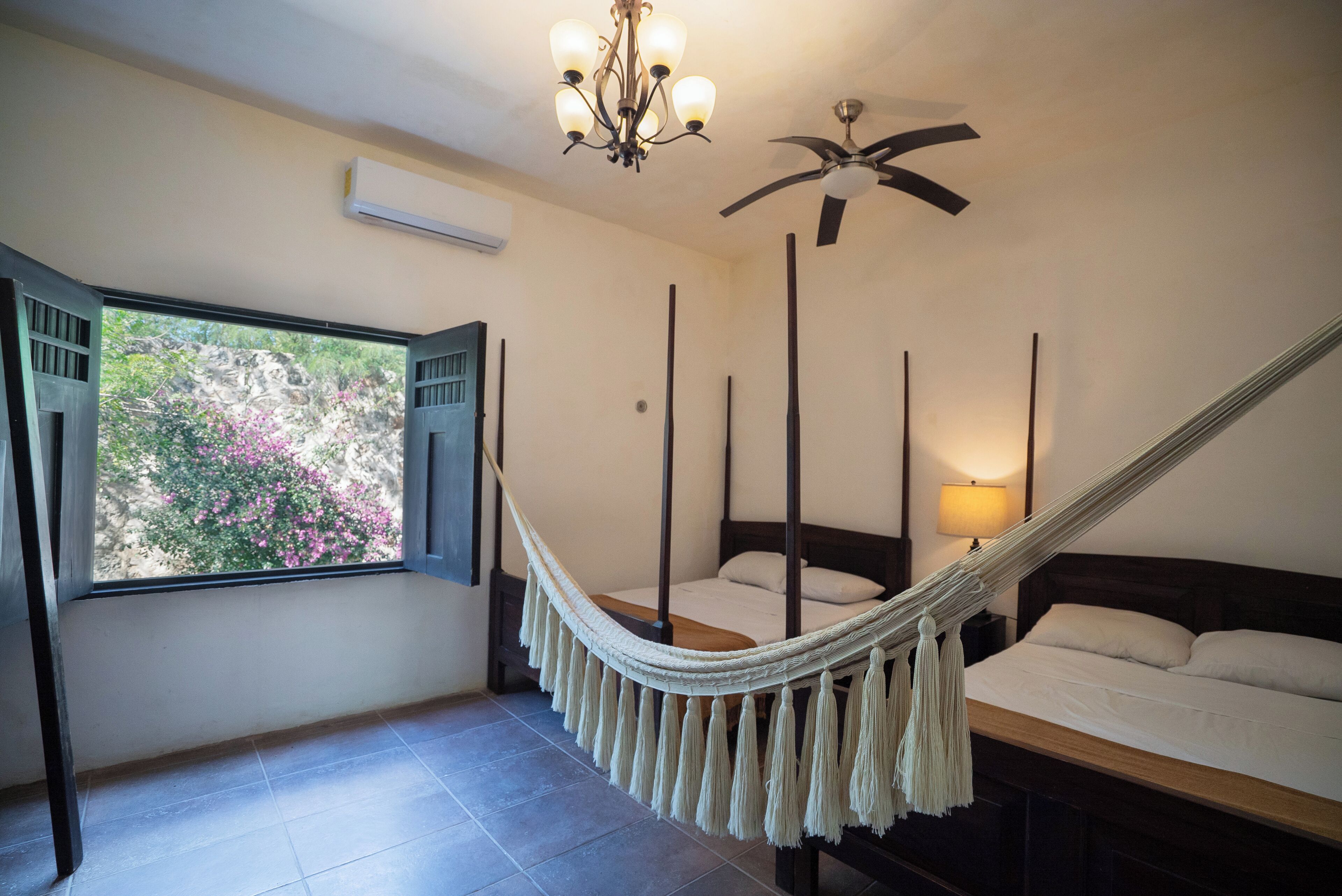 A bedroom with a bed, a hammock, a ceiling fan, and a window with shutters.