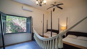 A bedroom with a bed, a hammock, a ceiling fan, and a window with shutters.