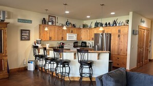 Een moderne keuken met houten kastjes, een roestvrijstalen koelkast en een bar met krukken.