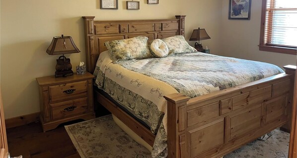 Een houten bed met een bloemenprint deken en twee kussens, een nachtkastje met een lamp en een klein bijzettafeltje met een zakdoos.