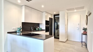A modern kitchen with a central island, built-in appliances, and a view into the adjacent living area. - SR Calanova Golf 2BDR with private garden (Mijas)