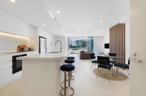 A modern kitchen with a central island, bar stools, and a dining area with a round table and chairs. - Luxury 2BR Palm Beach Apartment (Palm Beach)