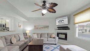 Una sala de estar con ventilador de techo, chimenea, sofá, mesa de centro y vistas al exterior.
