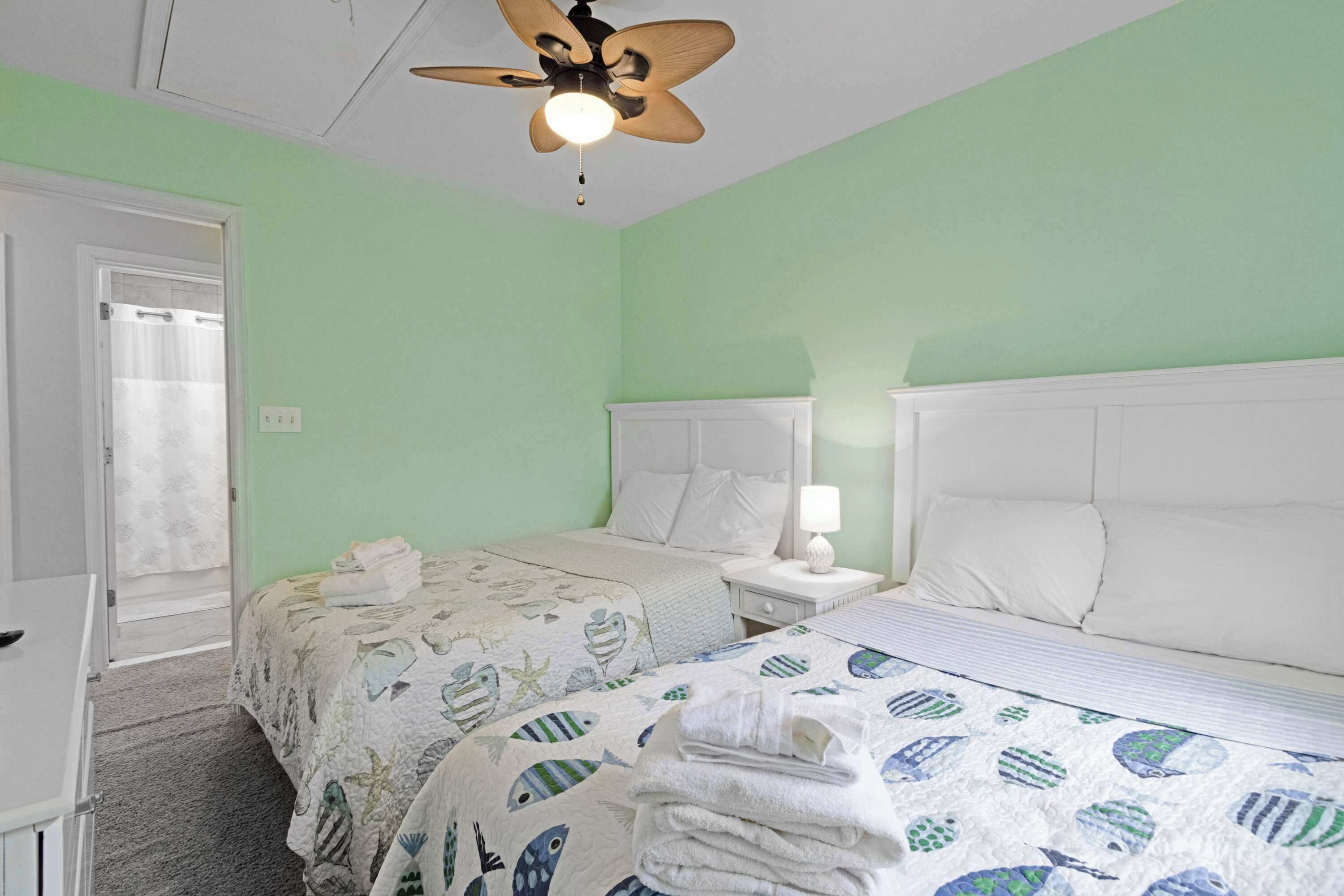 A hotel room with two beds, a ceiling fan, a nightstand with a lamp, and a door leading to a balcony.