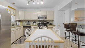Una cocina moderna con armarios blancos, un refrigerador de acero inoxidable, un microondas, una estufa y una mesa de comedor con sillas.