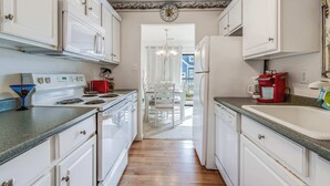 A kitchen with white cabinets, a stove, a microwave, a red coffee maker, and a sink. - Tiburon 1B (Ocean City)