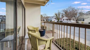 A balcony with wicker furniture and a potted plant, overlooking a residential street. - Tiburon 1B (Ocean City)