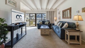 A spacious living room with a large window, a sofa, a coffee table, and a TV on a stand. - Tiburon 1B (Ocean City)