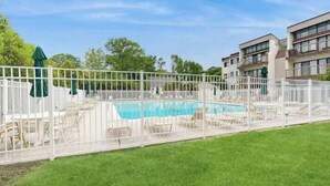 A swimming pool surrounded by a white fence, with lounge chairs and umbrellas. - Tiburon 1B (Ocean City)