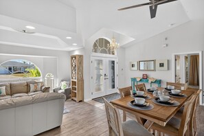 A spacious living area with a dining table set for six, a sofa, and a view of the outdoors. - Fin & Tonic~Heated Pool~Sleeps 12~Elegant Cape Coral Retreat (Cape Coral)