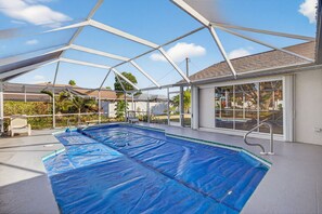An indoor swimming pool with a covered roof, clear glass walls, and a view of the surrounding neighborhood. - Fin & Tonic~Heated Pool~Sleeps 12~Elegant Cape Coral Retreat (Cape Coral)