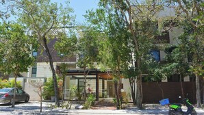 A modern building with a glass entrance, surrounded by trees and a parked scooter. - 🌴 Stylish 3-Bedroom Condo w/ Pool in Aldea Zama - Perfect for Families & Groups (Tulum)