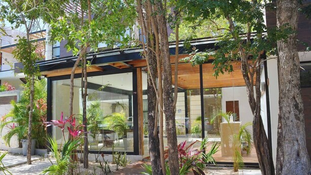 A modern building with large glass windows, surrounded by tropical plants and trees. - 🌴 Stylish 3-Bedroom Condo w/ Pool in Aldea Zama - Perfect for Families & Groups (Tulum)