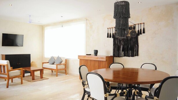 A spacious living room with a wooden dining table, comfortable seating, a flat-screen TV, and a large window providing natural light. - 🌴 Stylish 3-Bedroom Condo w/ Pool in Aldea Zama - Perfect for Families & Groups (Tulum)