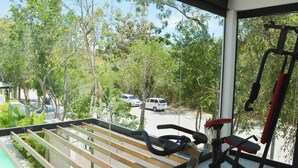 A balcony with a view of a parking area and trees, a pool, and exercise equipment. - 🌴 Stylish 3-Bedroom Condo w/ Pool in Aldea Zama - Perfect for Families & Groups (Tulum)