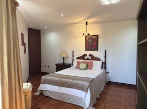 Quarto com cama, mesa de cabeceira, abajur e um quadro na parede.