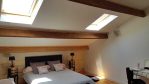A bedroom with a large bed, two bedside tables, a desk, and a chair. There are skylights on the ceiling. - Mas St-Jean: Charm, Climate & Garden in Provence (saint pierre de mezoargue)