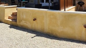 En bygning i sten med en terrasse, udendørs møbler og parasoller.