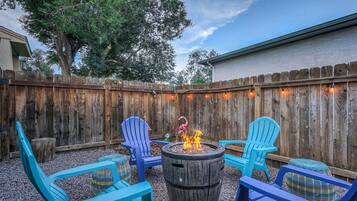A backyard with a wooden fence, a fire pit, and blue chairs.