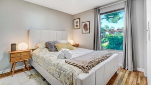 A bedroom with a bed, bedside tables, a window with curtains, and framed artwork on the wall. - 1014a Swope (Colorado Springs)