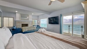 A bedroom with a bed, a ceiling fan, a fireplace, a TV, and a view of the ocean. - 1409 S Pacific Street (Oceanside)
