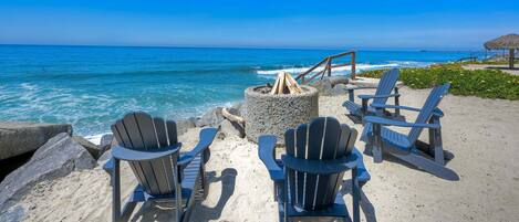 A beach view with chairs and a fire pit.